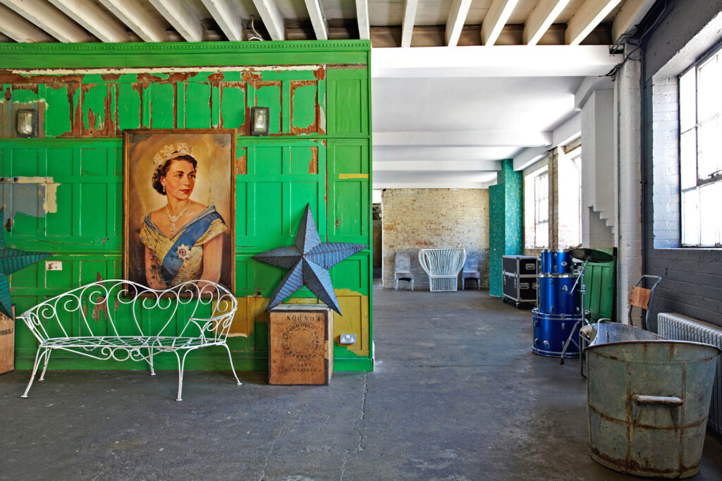 London warehouse space with bright green wooden cladded wall divider. Portrait of the queen centred in the middle of the wall next to giant paper star.