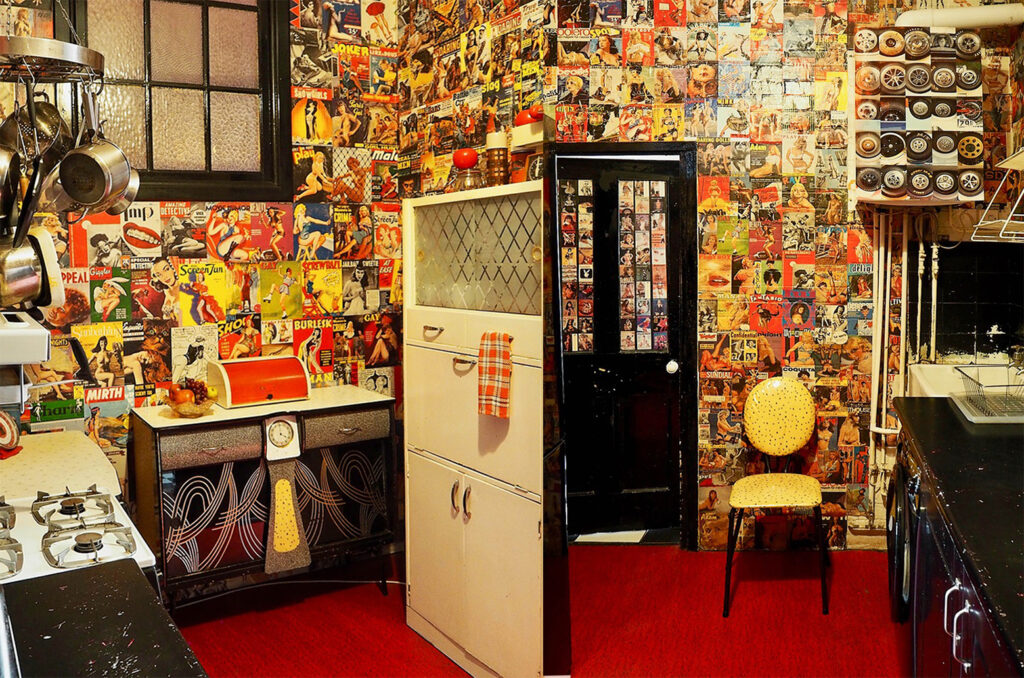 London retro kitchen with black appliances and gas hob. Vintage magazine covers plaster the walls.