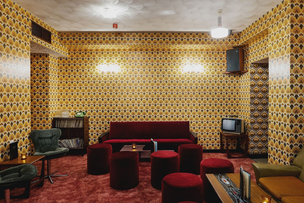 70's bar with red velvet sofa and mustard yellow wallpaper, wallpaper has intense repeated floral pattern.